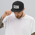Man wearing a black Christian cap with a SON logo on a rooftop with cityscape in the background